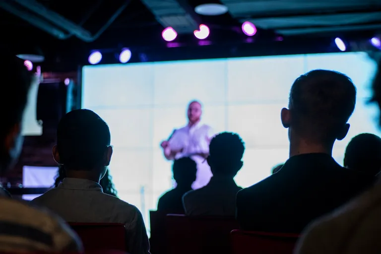 Audience watching a speaker on a bright screen